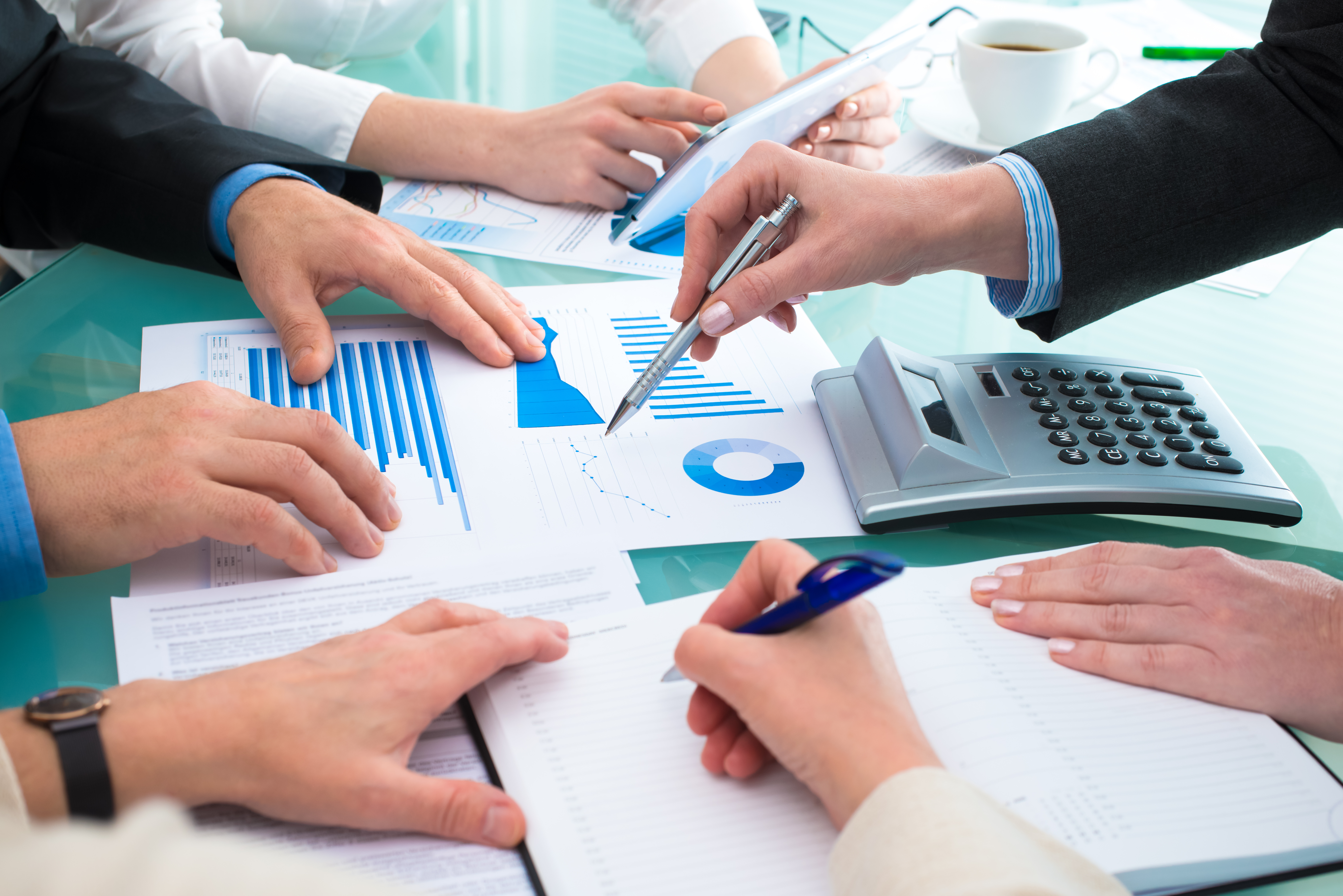 Business people as seen around a table but just their hands looking at what appears to be financial papers, and with a calculator, reflecting increased billing and career progression coaching for solicitors