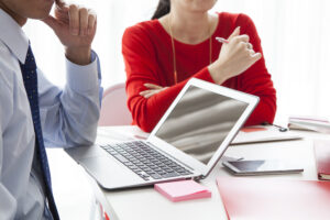 A male and female sat at a desk with a laptop between them, seemingly listening to a third person. Intended to reflect training for solicitors and legal executives looking to step into a management role.