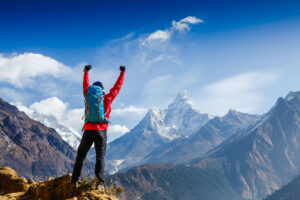 A mountain climber punching the sky with both hands at the top of a mountain which views of other mountains. Intended to demonstate reaching goals following great management training as a lawyer.