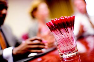 Three people at a table blurred out, with pens at the front and one person reaching for them. Inteded to reflect training for disciplinary and performance management training for solicitors and legal executives.