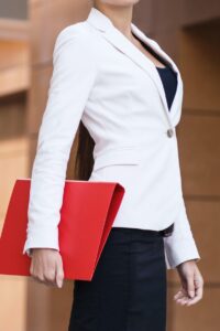 Female partner of a law firm dressed in a white jacket, black dress, and carrying a red folder, intended to reflect attending leadership and management training for solicitors.