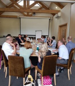 Groups of people around large round tables with pens and papers talking, they are attending a workshop. Reflecting training for solicitors and other lawyers.