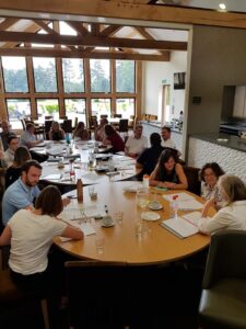 Image of a large group of people sat at large round tables at a venue with big widows. They are attending a training event with papers and pens on the tables. Reflecting training for lawyers and fee earners.